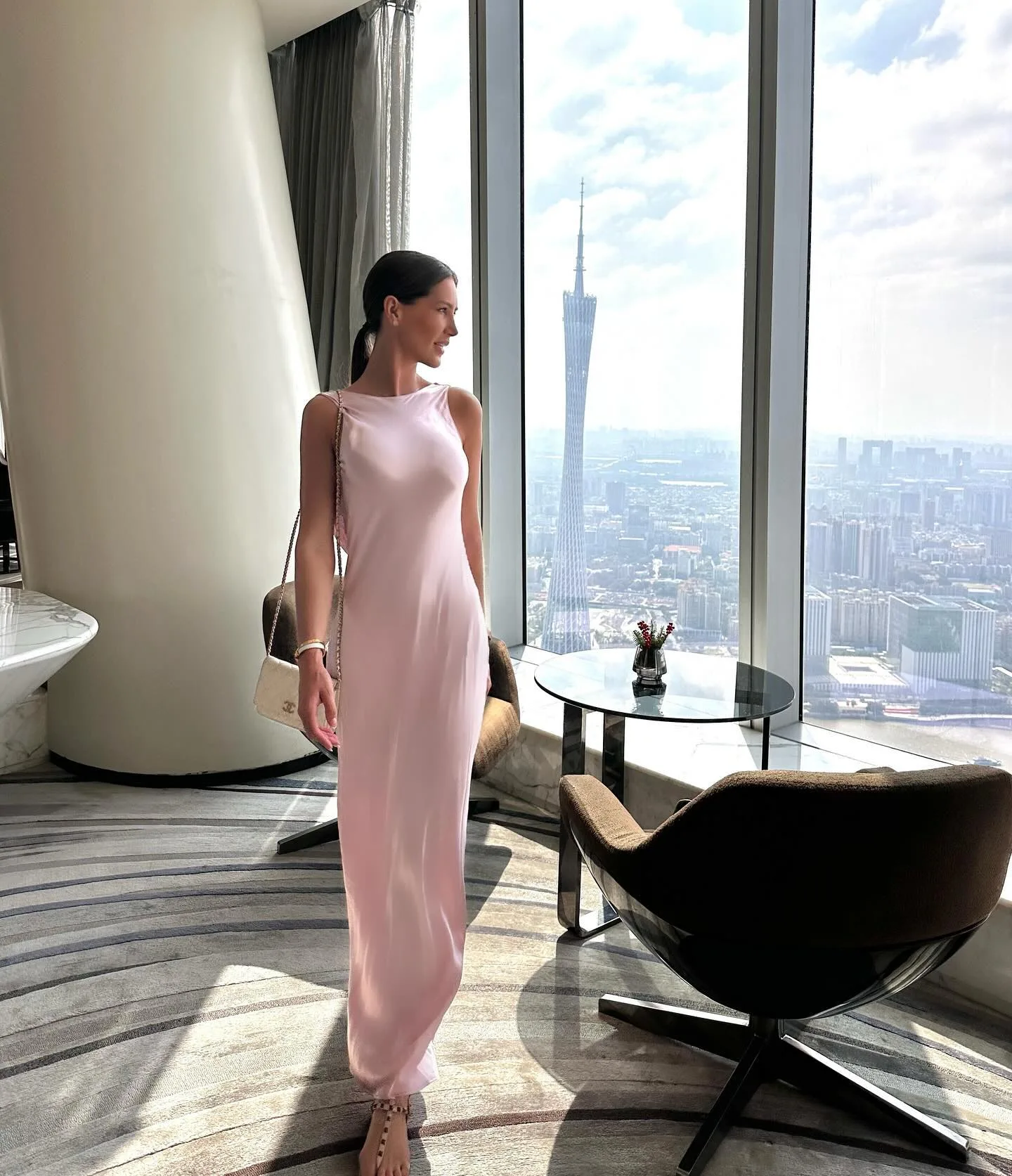 Giovanna de vestido rosa no Rosewood Guangzhou, com a Canton Tower na janela